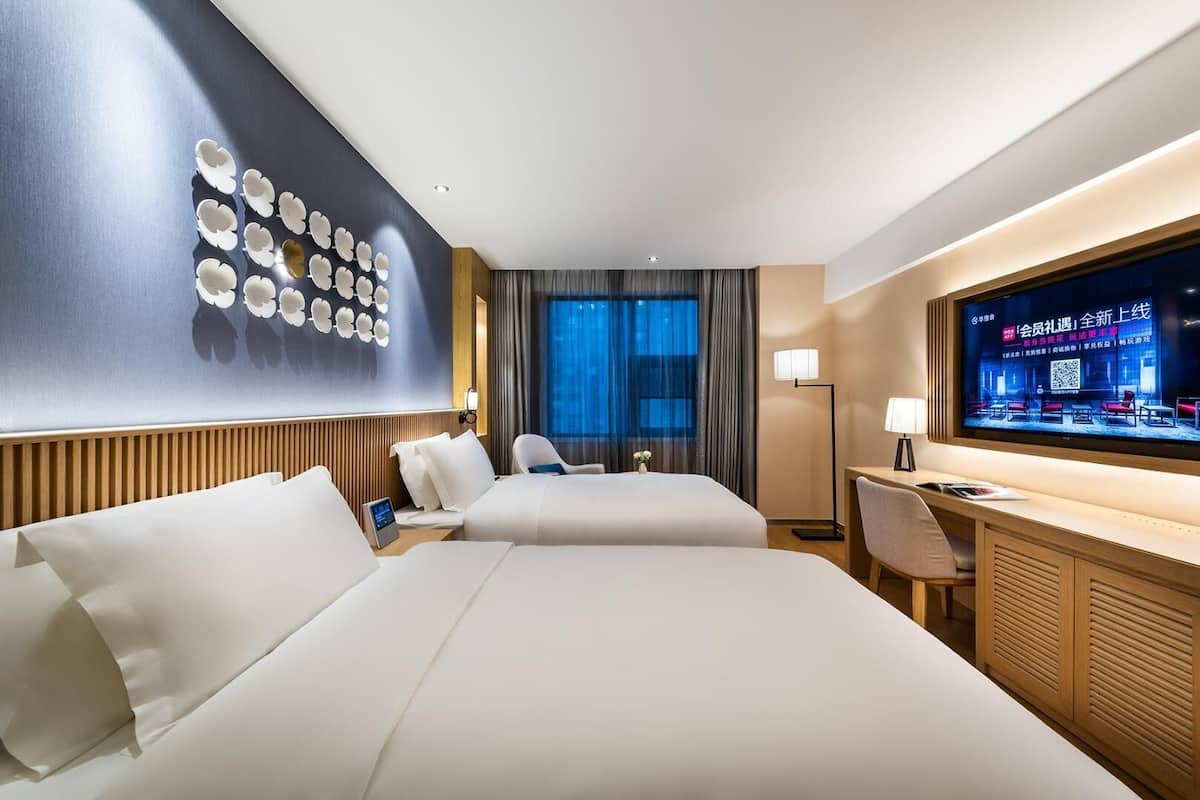 Hotelkamer met twee bedden, een bureau, een televisie en een wand met bloemenpatroon.