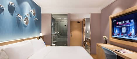 Una habitación de hotel con una cama grande, un escritorio, un televisor y una zona de ducha con paredes de vidrio.