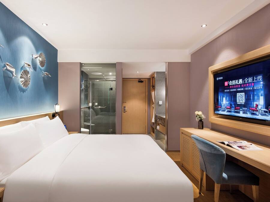 Una habitación de hotel con una cama grande, un escritorio, un televisor y una zona de ducha con paredes de vidrio.