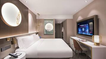 Habitación de hotel moderna con una cama grande, un escritorio con silla, un televisor y un espejo redondo.