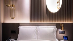 Een moderne hotelkamer met een groot bed, twee nachtkastjes, een rond wandlamp en een wandpaneel met verticale lijnen.