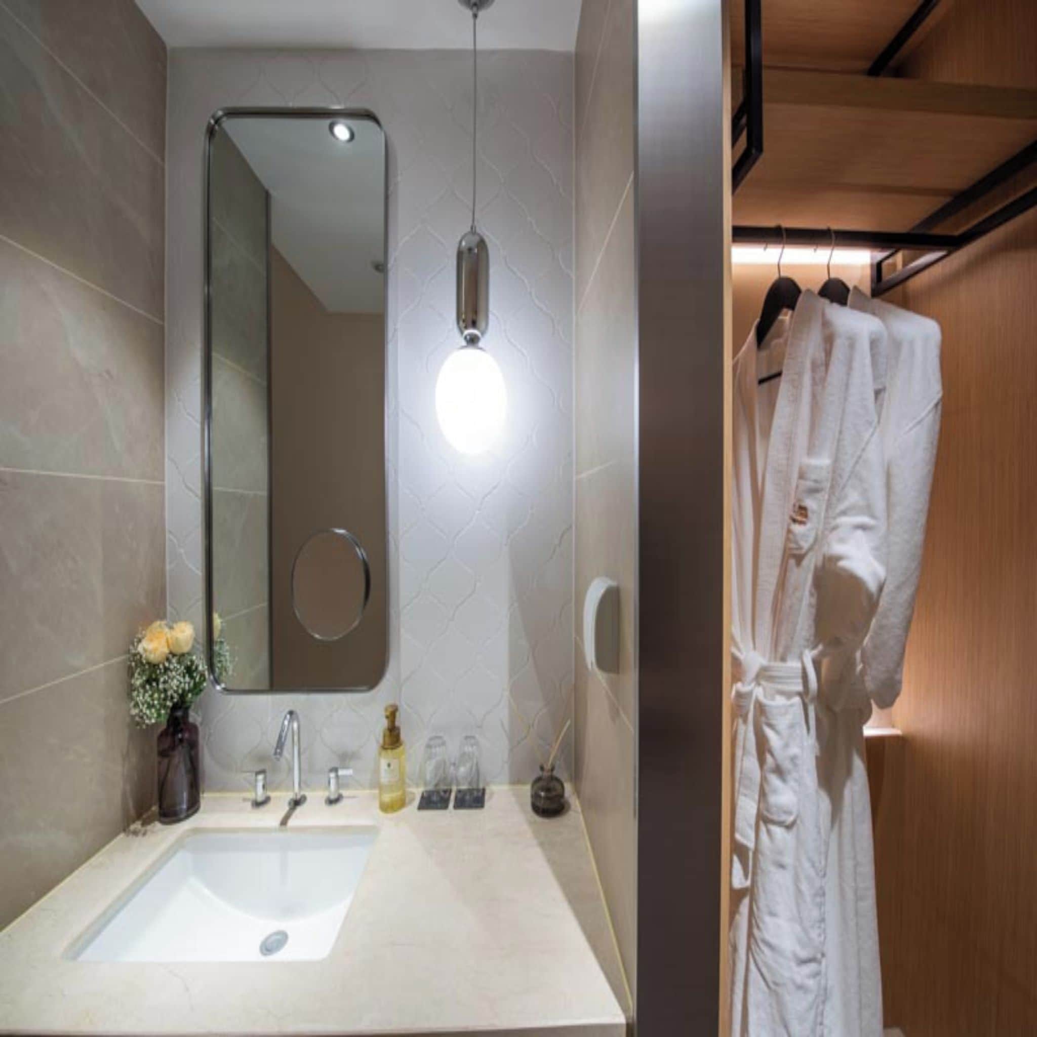 Een moderne badkamer met een grote spiegel, een wastafel en een badjas die aan een rek hangt.