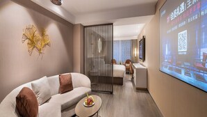 Quarto de hotel moderno com sofá, uma pequena mesa com frutas, uma tela de projetor exibindo uma apresentação e uma porta deslizante que dá para outro quarto.