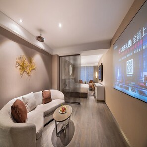 A modern hotel room with a sofa, a small table with fruit, a projector screen displaying a presentation, and a sliding door leading to another room. - Crystal Orange Hotel Changsha Furong Road IFS (Changsha)