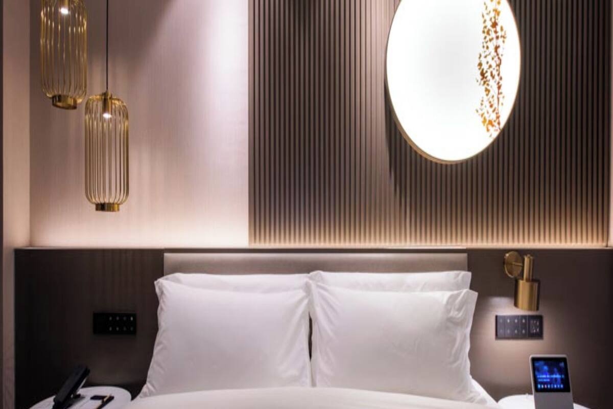 Een moderne hotelkamer met een groot bed, twee nachtkastjes, een rond wandlamp en een wandpaneel met verticale lijnen.