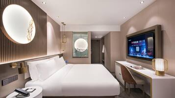 Una habitación de hotel moderna con una cama grande, un escritorio, un televisor y un espejo.