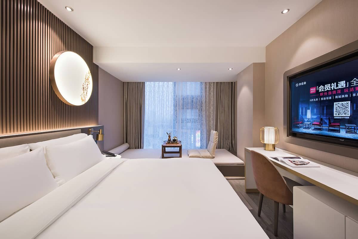 Een moderne hotelkamer met een groot bed, een bureau, een televisie en uitzicht op de stad door het raam.