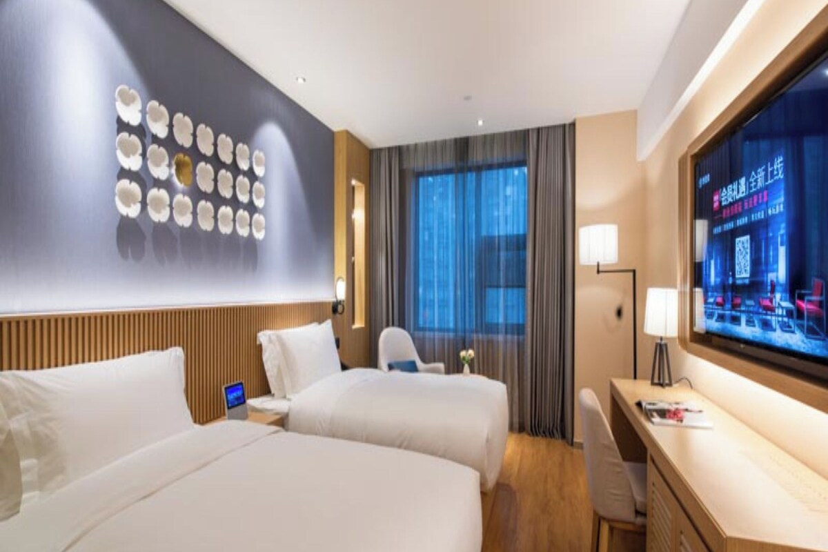 A hotel room with two beds, a desk, a TV, and a wall with decorative plates.