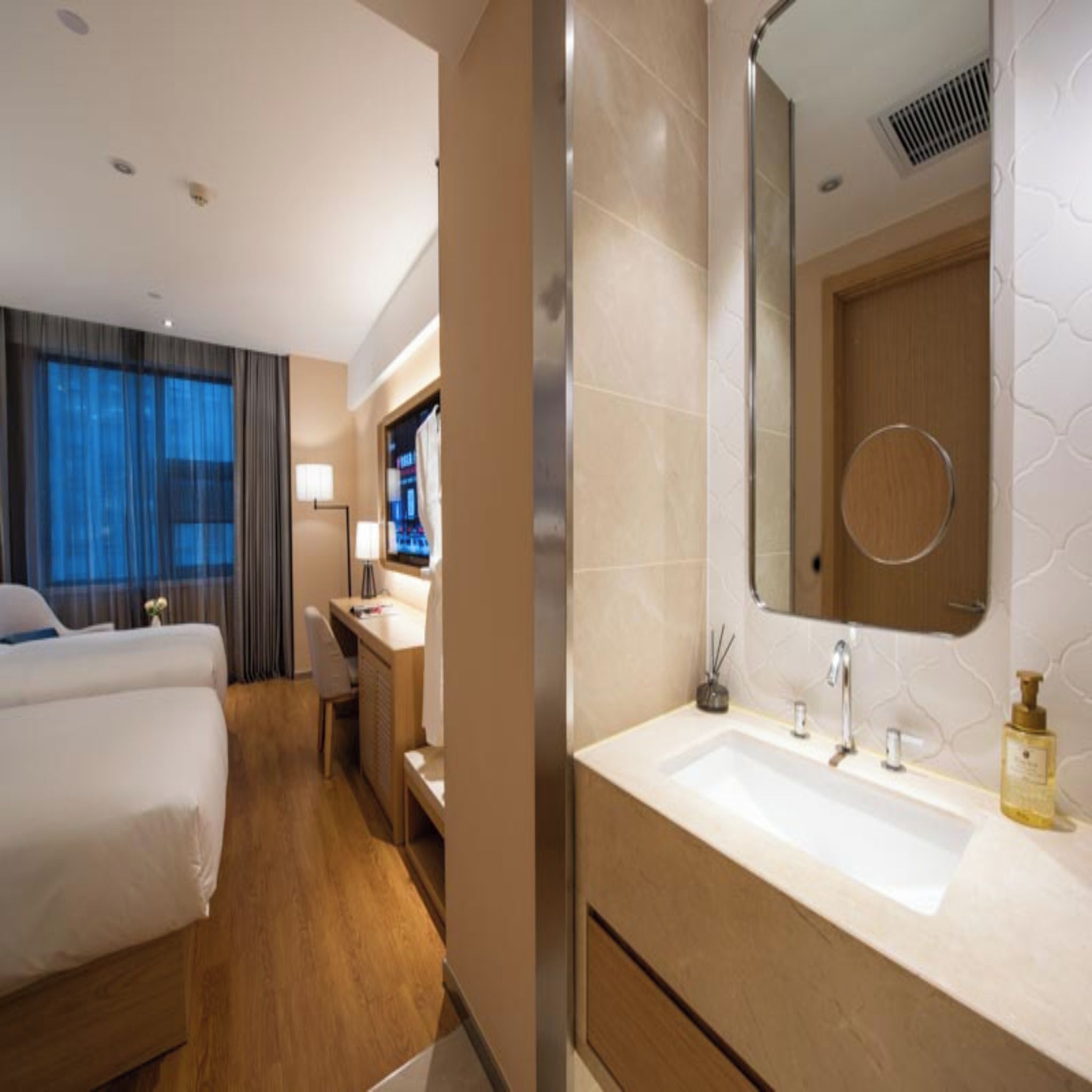 A hotel room with a bed, a desk, a bathroom with a sink and mirror, and a TV.