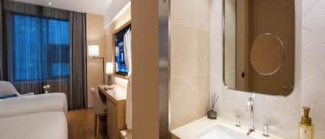 A hotel room with a bed, a desk, a bathroom with a sink and mirror, and a TV.
