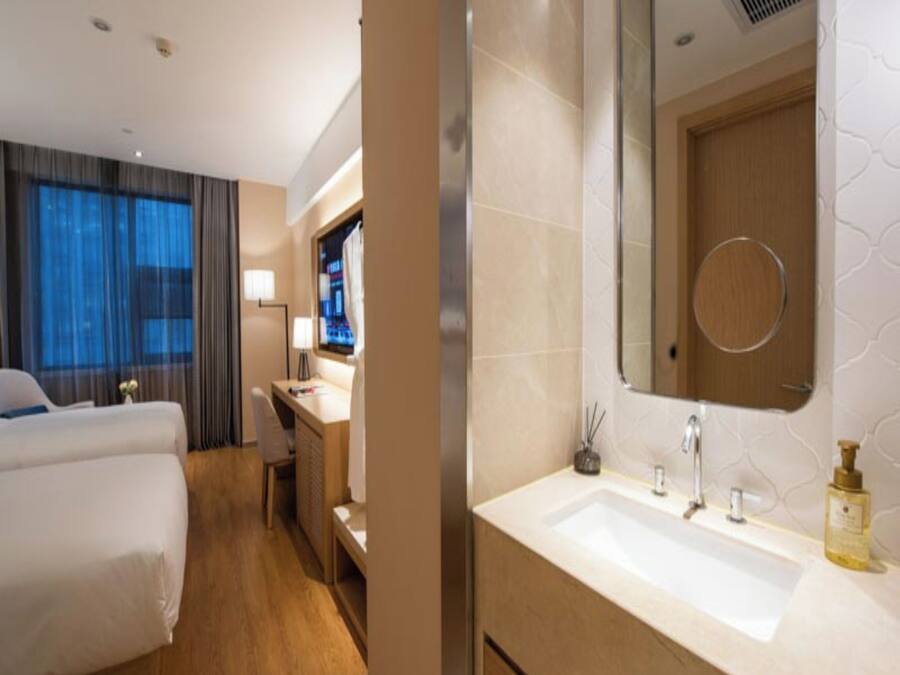 Habitación de hotel con cama, escritorio, baño con lavamanos y espejo, y televisión.