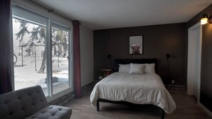 A bedroom with a large window, a bed, a chair, and a small table. - One Bedroom Condo Near Whyte Ave (Edmonton)