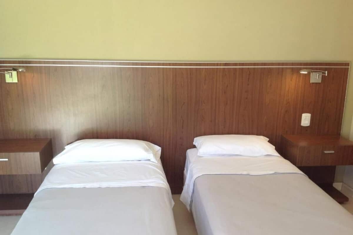 A hotel room with two single beds, wooden headboard, and bedside tables.