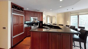 A modern kitchen with dark wood cabinets, stainless steel appliances, and a central island with bar stools. - Liftside 3BR ~Unit C42~ Ski-in-Ski-out Chair #20 (Vail)