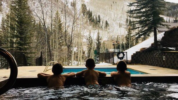 A pool area with three people sitting by the edge, overlooking a snowy mountain landscape. - Liftside 3BR ~Unit C42~ Ski-in-Ski-out Chair #20 (Vail)