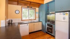 A kitchen with wooden ceiling beams, a window, a sink, a stove, and a refrigerator.