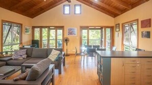 A spacious living area with a high ceiling, wooden beams, a sofa, a dining table, and a kitchen area.