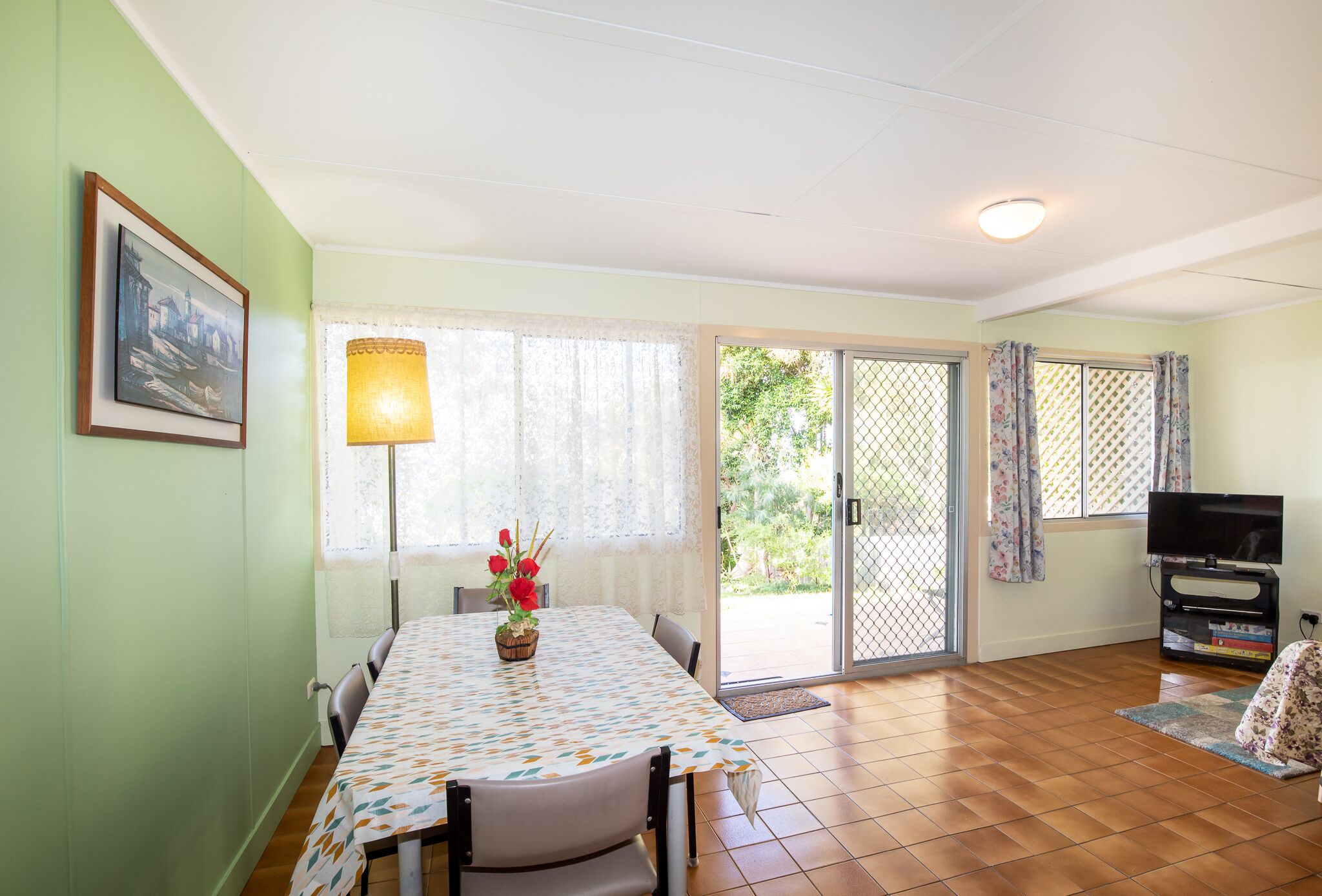 A dining area with a table, chairs, a lamp, and a TV.