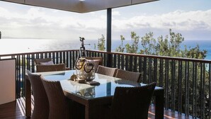 A balcony with a glass table and wicker chairs, overlooking a scenic ocean view. - Banyandah - Breathtaking views (Point Lookout)