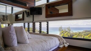 A bedroom with a large bed, a TV mounted on the wall, and a view of the ocean. - Banyandah - Breathtaking views (Point Lookout)
