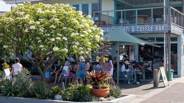 Ein Café mit Außenbestuhlung, ein großer Baum und ein Schild mit der Aufschrift 'Café & Coffee Bar'.