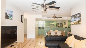Ein modernes Wohnzimmer mit einem Flachbildfernseher, einem schwarzen Ledersofa, einem Holztisch und zwei Deckenventilatoren.