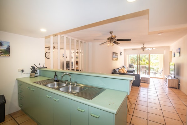 A kitchen with a large island, double sink, and a dining area with a sofa and TV.