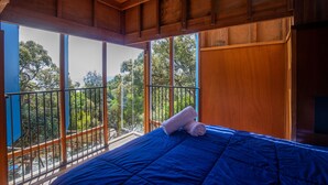 A room with a large bed, wooden ceiling, and a balcony with a view of trees.