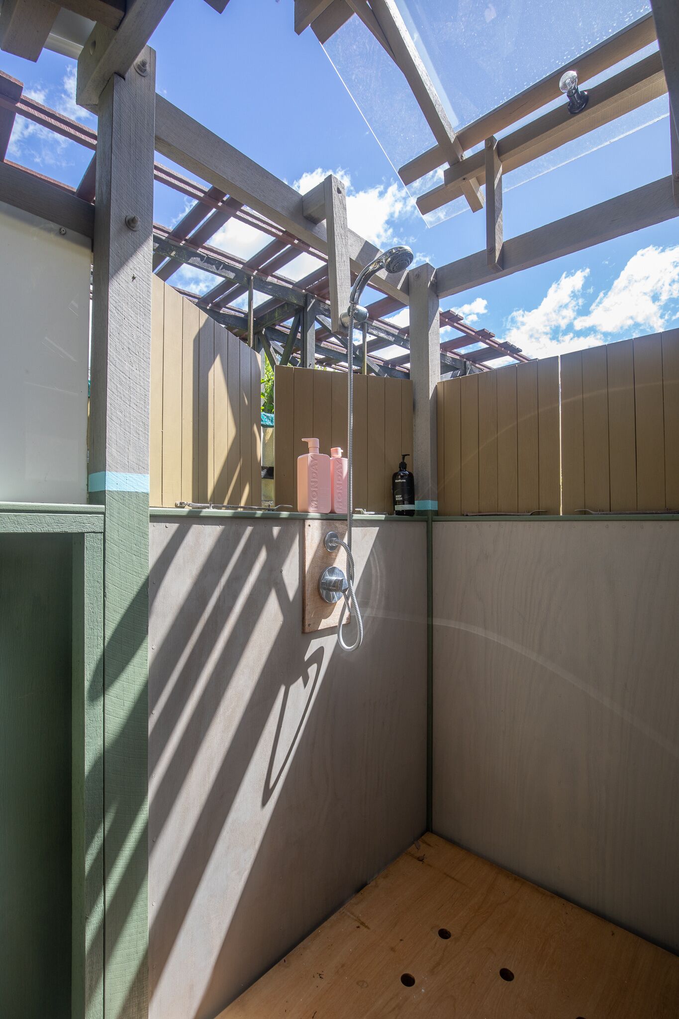 A small, enclosed shower area with a wooden floor and a metal showerhead.