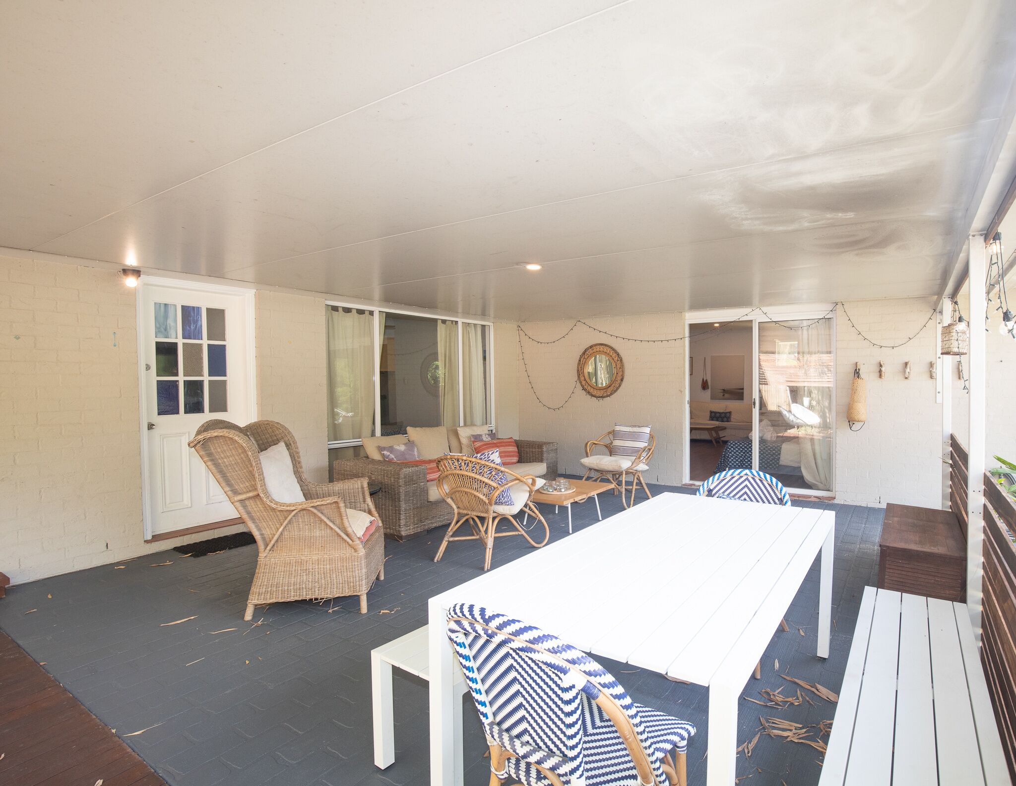 Un espace extérieur aménagé en terrasse, avec des meubles en osier, une table blanche et une vue sur l’intérieur de la maison.
