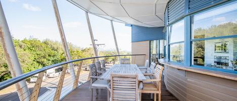 Eine Holzterrasse mit Tisch und Stühlen mit Blick auf eine Straße und Grünflächen.