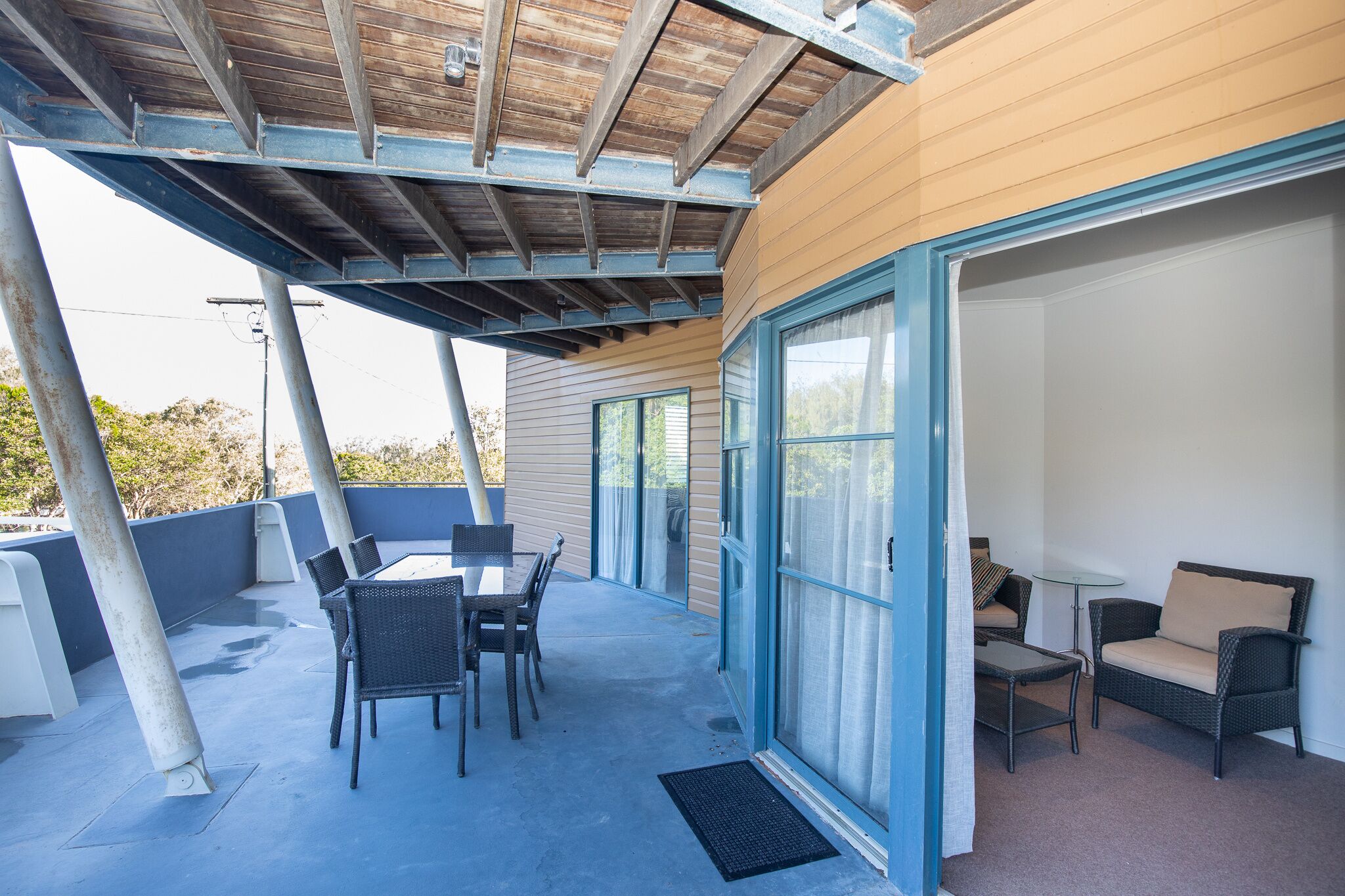 An outdoor patio with a table and chairs, a small table with a chair, and a wicker sofa.