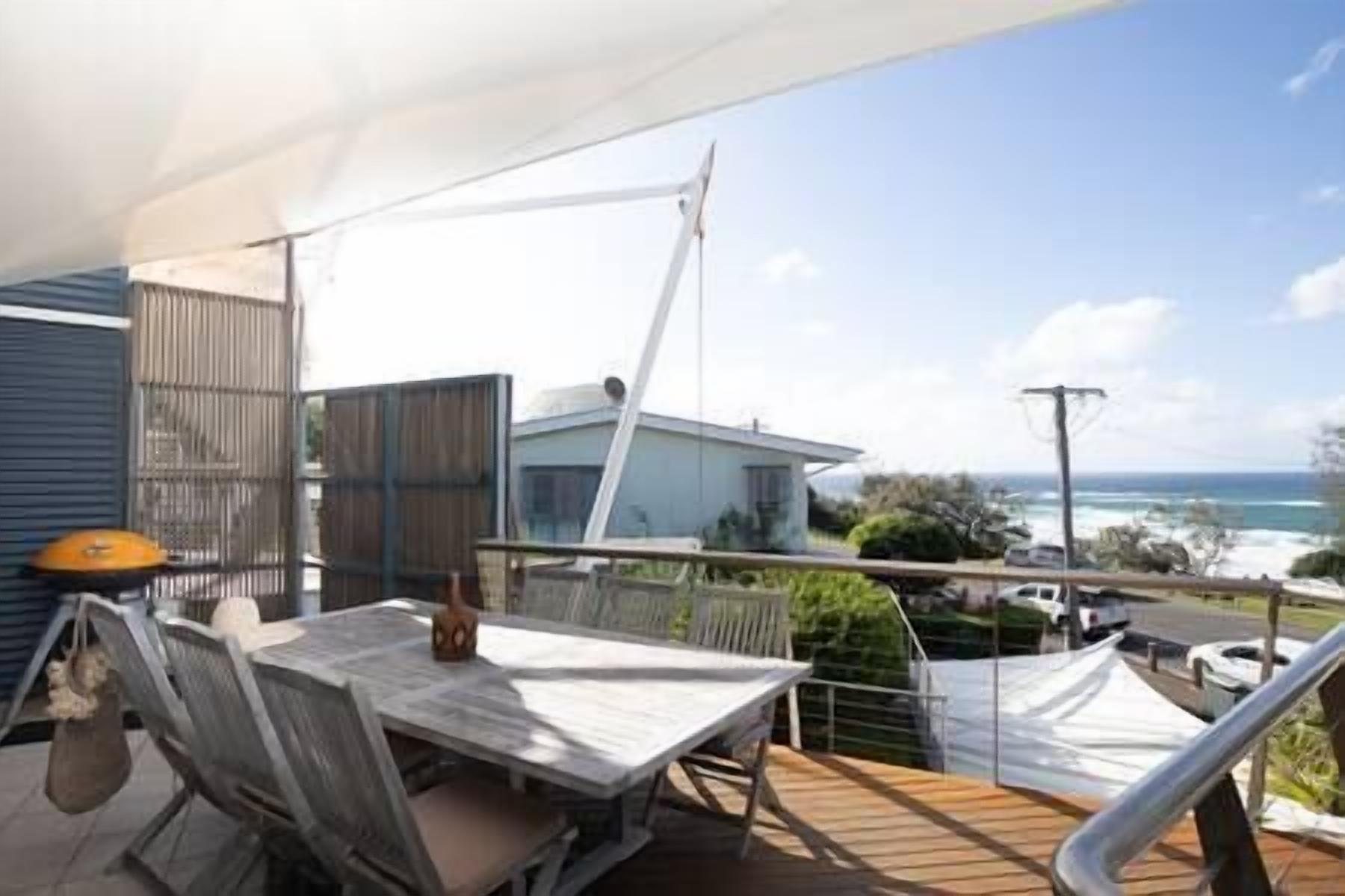 A balcony with a table and chairs, overlooking a residential area and the ocean.