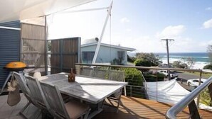 Un balcon avec une table et des chaises, donnant sur un quartier résidentiel et l’océan.
