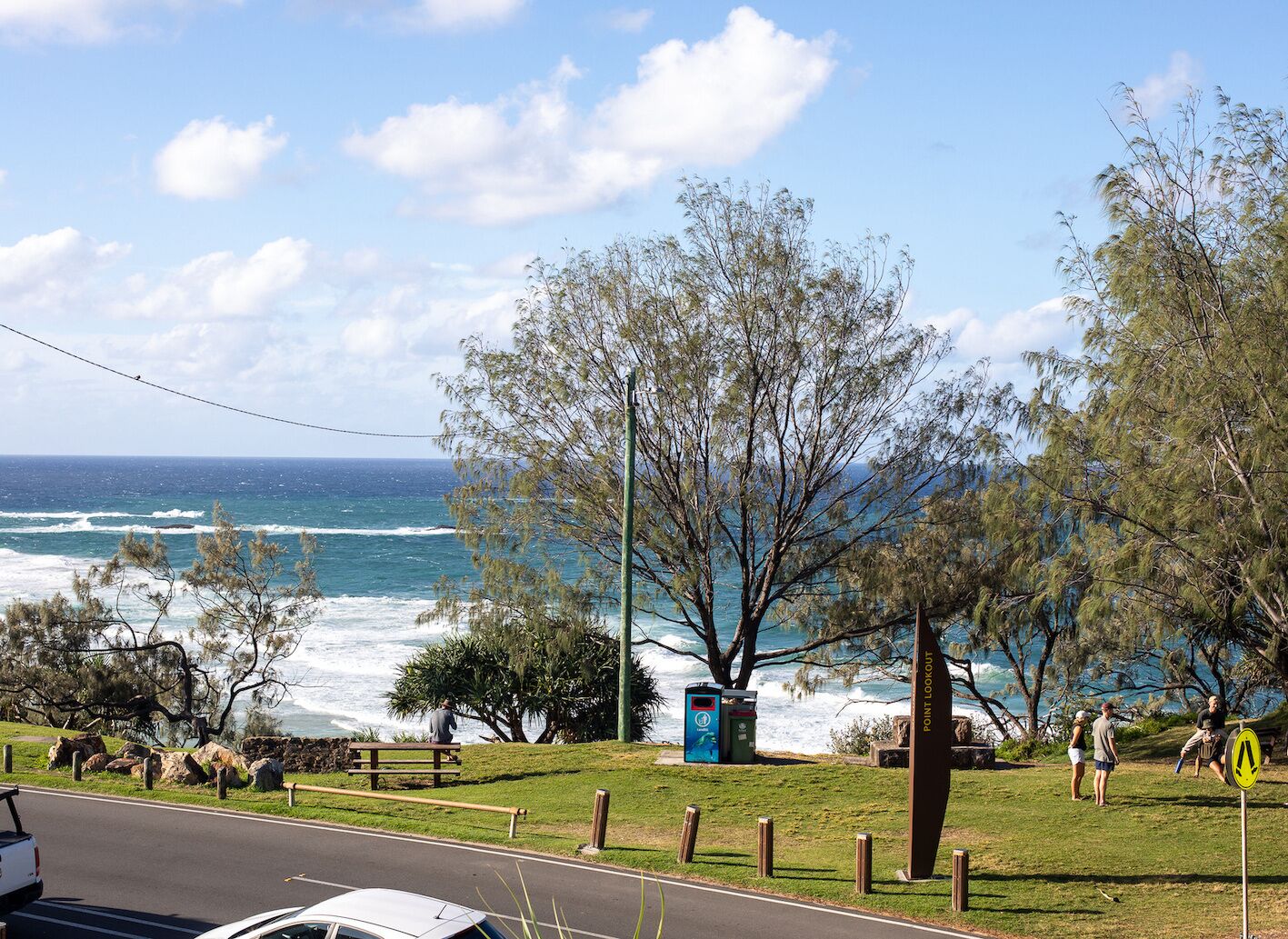 A coastal viewpoint with a bench, trees, and a sign indicating a lookout point.