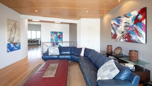 Un salon moderne avec un canapé d’angle en cuir bleu, un tapis rouge et des œuvres d’art abstraites accrochées aux murs.