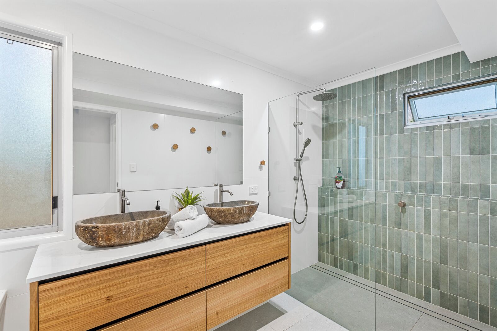 A modern bathroom with two stone sinks, a wooden vanity, a glass shower enclosure, and a large mirror.