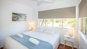 Quarto com cama, ventoinha no teto, janela com vista e luminária de cabeceira.
