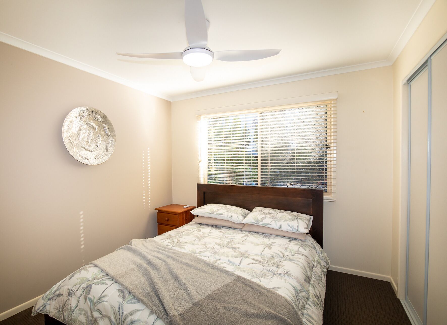 A bedroom with a bed, a nightstand, a ceiling fan, and a window with blinds.
