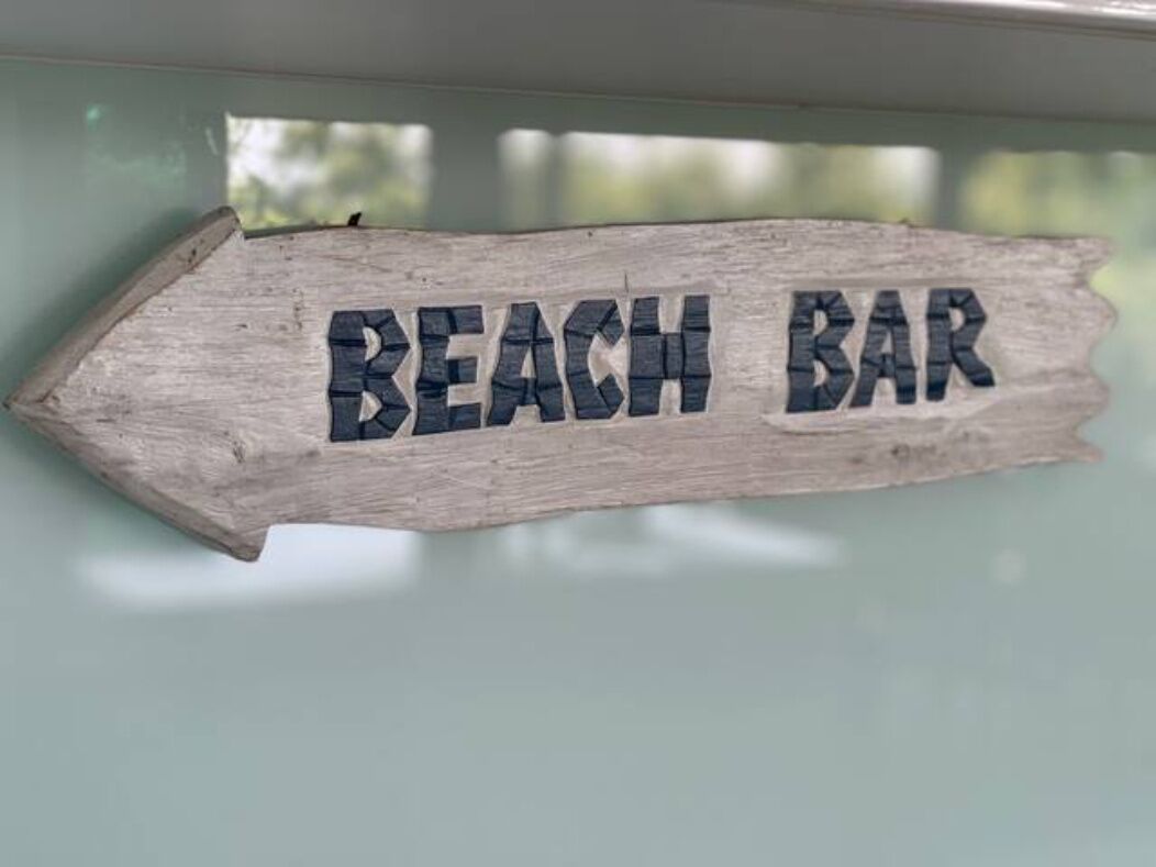 Een houten bord met de tekst 'BEACH BAR'.
