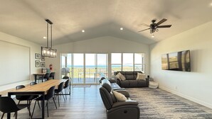 A spacious living area with a dining table, chairs, a sofa, and a large window offering a view of the outdoors.