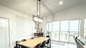 A modern dining area with a wooden table and black chairs, a ceiling light fixture, and a view through large sliding doors to an outdoor deck.