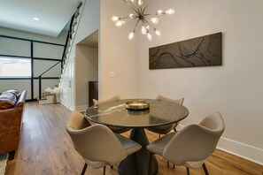 Comedor con una mesa redonda, cuatro sillas, una araña y una escalera moderna.