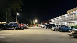 Un parcheggio con diverse auto, un edificio a più piani e un albero sullo sfondo.