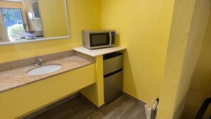 Un bagno piccolo con una parete gialla, un lavandino, uno specchio, un forno a microonde e un frigorifero in acciaio inossidabile.