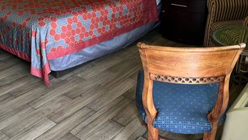 Una habitación de hotel con una cama, una silla de madera y una mesita de noche.