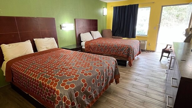 Una camera d'albergo con due letti, pavimento in legno, parete verde e parete gialla.