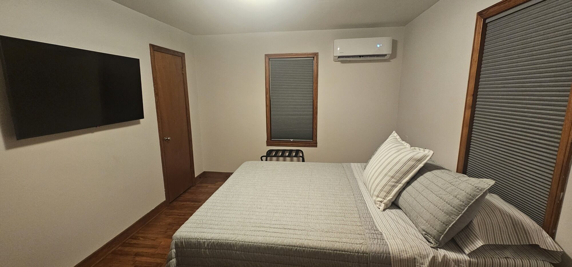 Quarto com cama, televisão na parede, ar condicionado e janela com persianas.