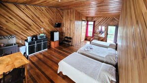 A cozy, wooden-paneled room with two beds, a kitchenette, and a dining area. - Cabinas Selva Verde (Monteverde)