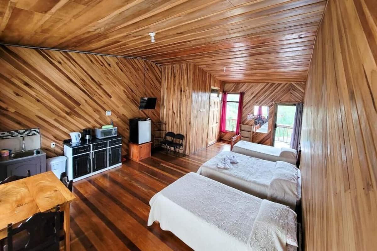 A cozy, wooden-paneled room with two beds, a kitchenette, and a dining area.